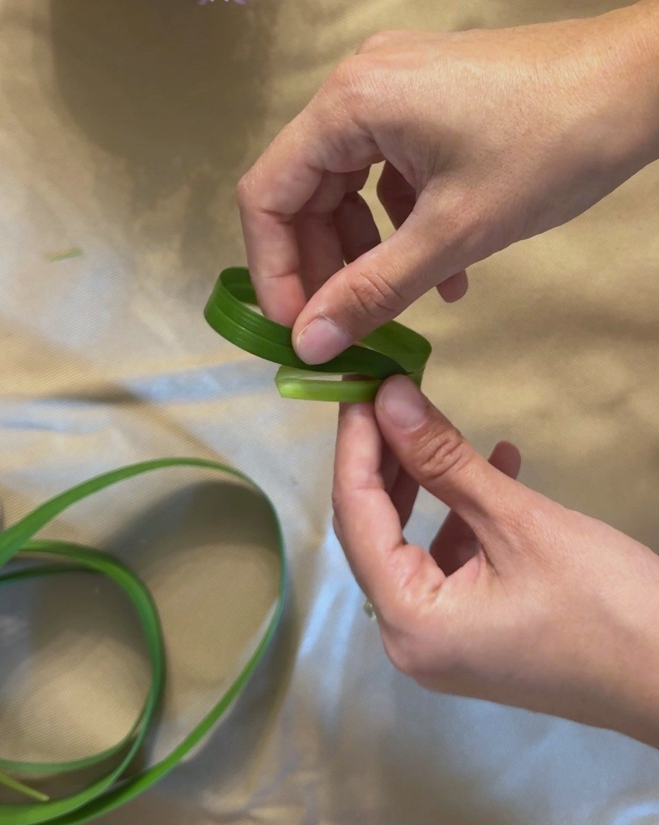 Hands working a strap leaf into a loop on a paper-covered bench.